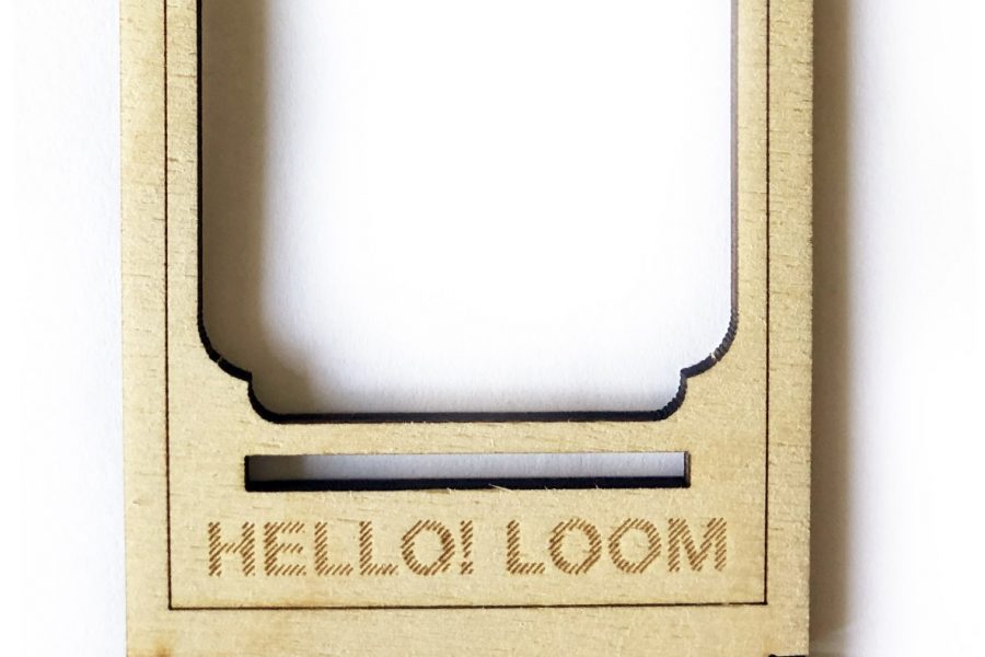 Photograph of a miniature wooden hand-held loom with words "Hello Loom"