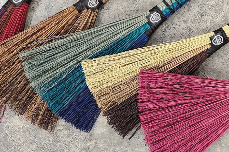5 hand made, hand held brooms placed on concrete floor,