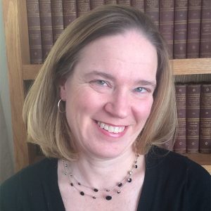 Photo of a woman with shoulder length, blonde hair in front of a bookcase and wearing a black top smiling at the camera