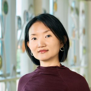 Photo of Esther Kang, woman at bust length with short black hair and a dark red shirt looking at the camera with a slight smile.