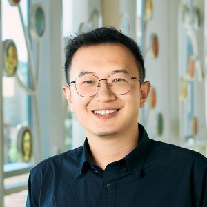 Photo of Yaoyi Zhou, man a portrait height wearing a dark shirt and glasses, smiling at the camera.