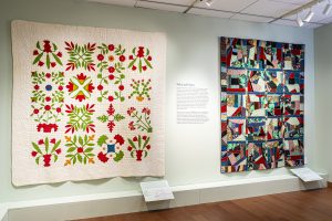 Photo of a gallery with green walls and two large quilts hanging on the wall with labels in front of them