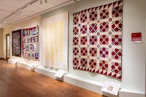 Photo of an art gallery with quilts on a wall.