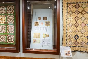 Photo of a glass case showing several fragments of quilts on a blue background.