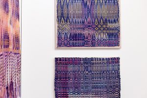 A close-up photo of purple, blue, orange, and pink textiles against a white wall.