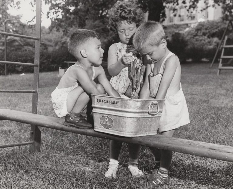 "Children stick their hands into a "wheeling" bucket on a playground at the UW Nursery School."