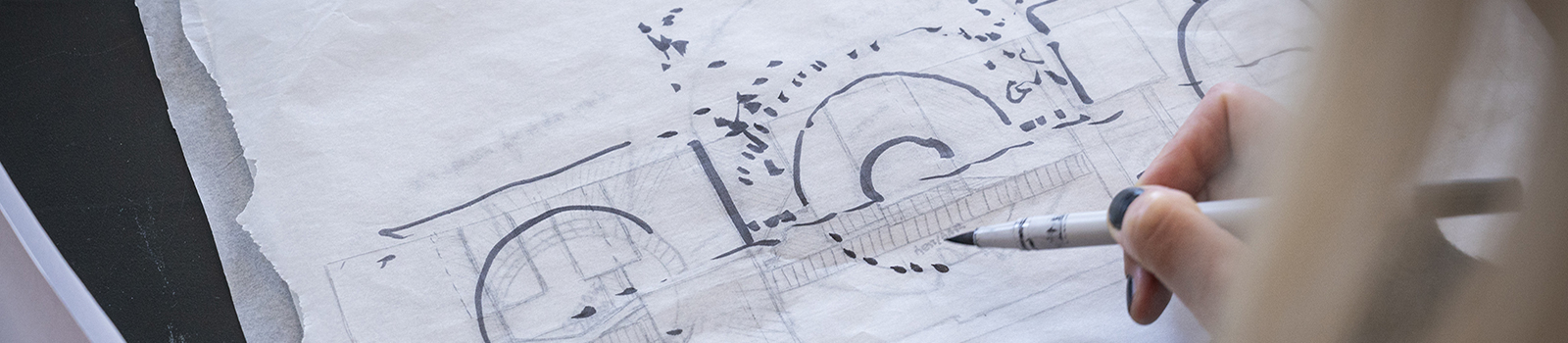 Image over the shoulder of a person drawing on a white piece of paper with a black ink pen