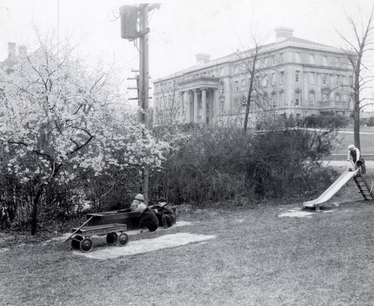 "Several children play on a slide and in a sandbox in the Dorothy Roberts Nursery School playground at the school of Home Economics."