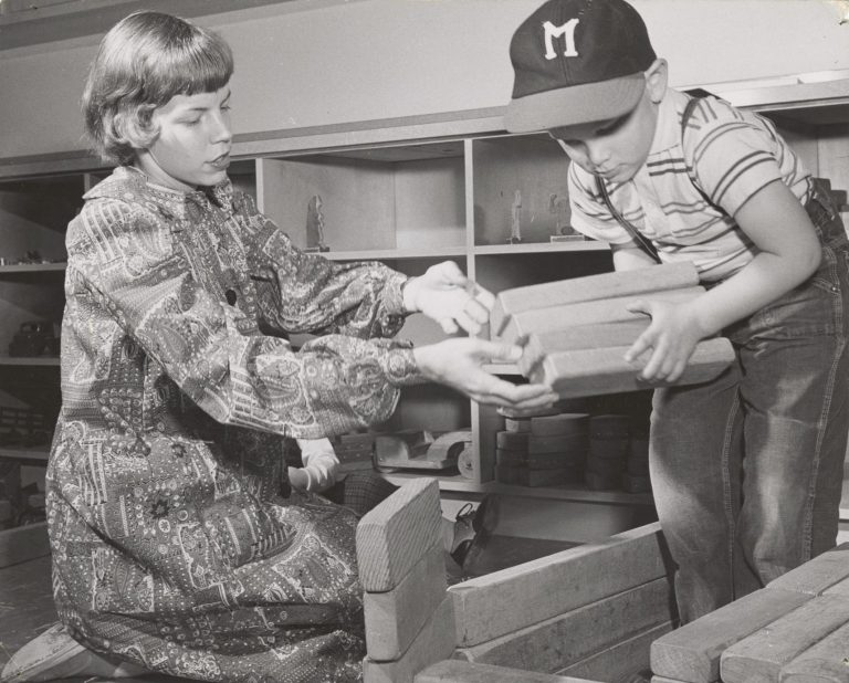 "Four-year-old Mike, son of Mr. and Mrs. John G. Mueller, gets building help from Lana Gerhardt, graduate student from Short Hills, NJ. Blocks are stored in built-ins."
